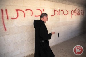A priest walks past a graffiti reading in Hebrew "idols will be cast out" as he inspects the damage at the Church of the Multiplication at Tabgha, on the shores on the Sea of Galilee in northern Israel, on June 18, 2015. (AFP/ Menahem Kahana)
